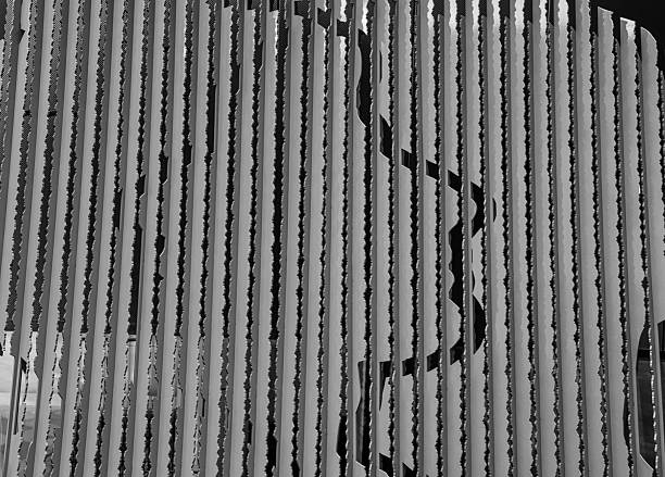 monochrome abstract photograph capturing a hidden silhouette behind vertical metallic slats. The interplay of shadows, textures, and repeating lines creates a striking contemporary composition that blends industrial design with fine-art minimalism. Ideal for creative, architectural, and conceptual visual projects.