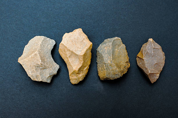 Primitive Stone Age flint tools and artifacts lying on a dark surface, representing prehistoric human technology and early civilization