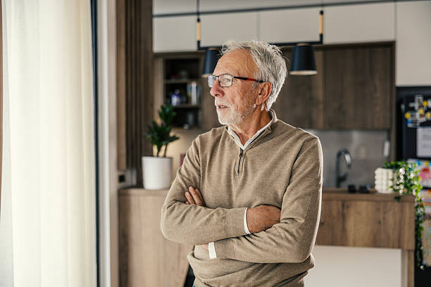 istock Senior man looking thoughtfully out window at home 2250498542