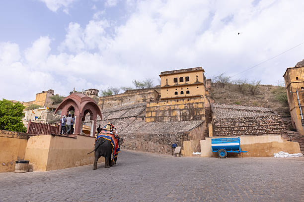 Jaipur, Rajasthan, India - April 2022: Portrait of unidentified tourist riding on decorated elephant at the premises of amber fort at jaipur. Architecture view of amber fort at background.