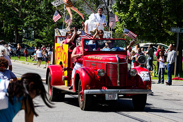 Rutland, Ma - July 04, 2009: Vintage red fire truck with Knutson logo drives down tree-lined street waving to crowd in patriotic parade. Spectators line sides of road capturing festive, nostalgic