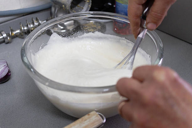 istock Hands whisk white cream in a glass bowl on a clean kitchen counter surface. 2250504970