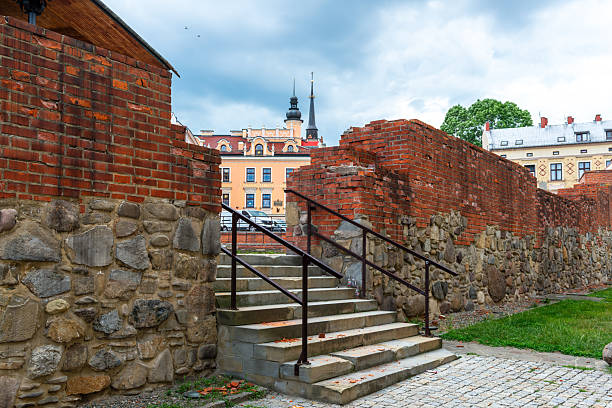 Tarnow, Poland – July 12, 2025: A historic brick and stone wall frames a set of exterior stairs, leading toward brightly painted townhouses in the distance. Architectural layers reveal the preserved character of the old city.