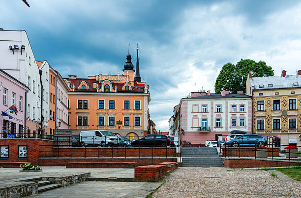 Tarnow, Poland – July 12, 2025: A curved cobblestone street lined with pastel townhouses and storefronts creates a charming urban scene. Outdoor cafés, trees, and decorative balconies emphasize the calm character of the historic district.