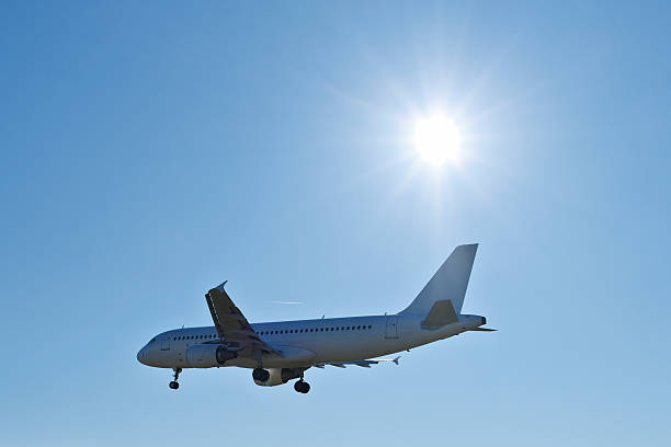 A white passenger airplane soaring high in the endless clear blue sky, crowned by a brilliant sun flare with radiant rays.