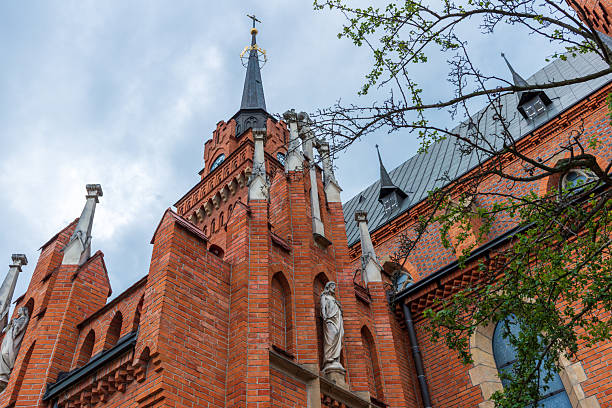 Tarnow, Poland – July 12, 2025: The red-brick facade of the Gothic Revival church rises with pointed towers and stone statues, emphasizing the dramatic architectural style and rich craftsmanship.