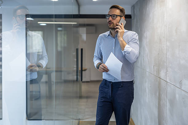 istock Businessman talks on the phone while holding documents in a modern office corridor during working hours 2250513936