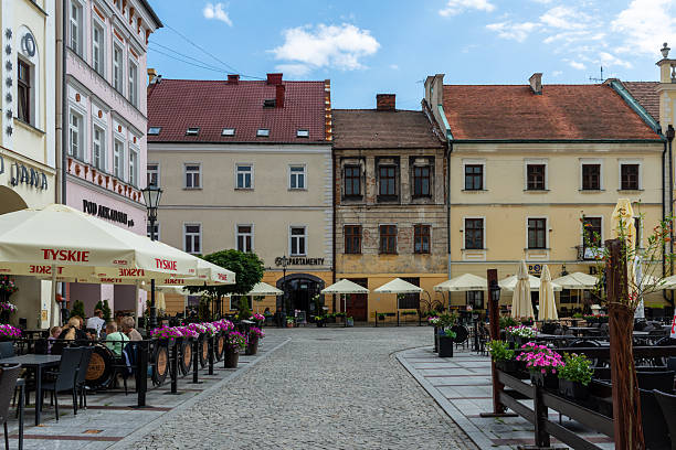 Tarnow, Poland – July 12, 2025: Restaurant terraces with branded umbrellas and blooming flowers line the cobblestone streets, creating a lively yet relaxed dining atmosphere in the historic center.