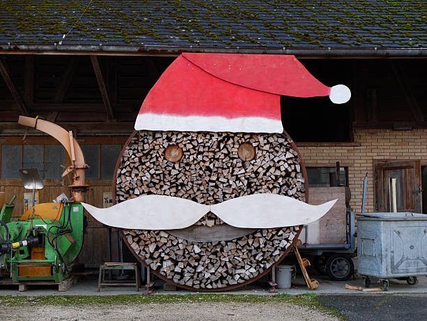 Creative Wood Storage Structure Decorated as Santa Claus with Red Hat, White Mustache and Circular Log Pattern Outside Rustic Barn. High quality photo A creative wood storage construction arranged to resemble Santa Claus, complete with a red hat, white mustache, and circular log pattern. The rustic setting and playful design create a festive, humorous outdoor decoration. Ideal for themes of Christmas, winter holidays, rural creativity, handmade decor, and seasonal celebrations.