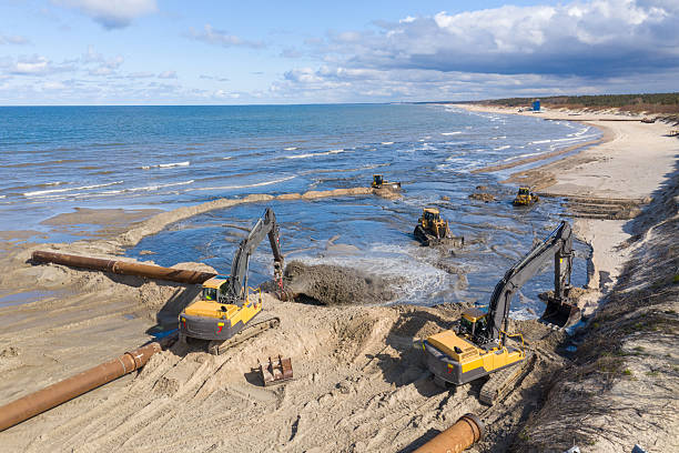 istock Beach restoration sand Bulldozers. Mud flows from the pipe with excavator behind for the reconstruction of the beach taken away by the sea. Work in progress for beach nourishment. Drone shot. 2250523037
