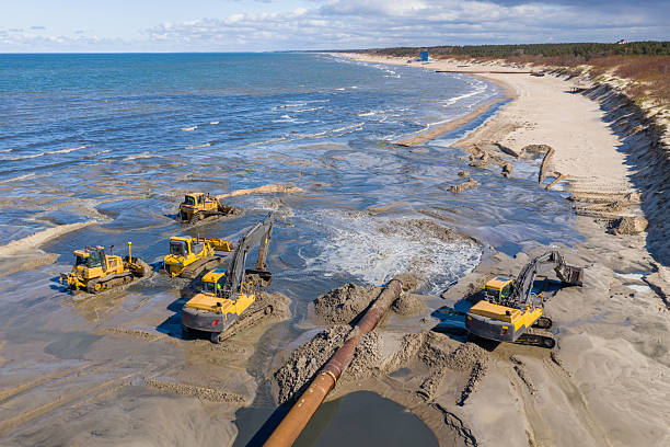 istock Beach restoration sand Bulldozers. Mud flows from the pipe with excavator behind for the reconstruction of the beach taken away by the sea. Work in progress for beach nourishment. Drone shot. 2250523105