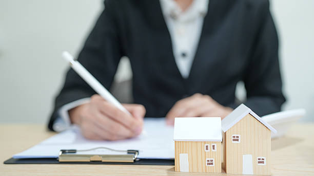 istock Businessperson Signing Documents with Miniature House Models on Desk in Office Setting 2250525100
