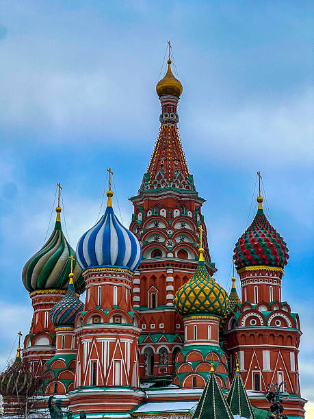 The detailed shot highlights the intricate patterns, textures, and vibrant colors of the domes, including the distinctive blue and white stripes, the green and yellow diamond patterns, and the deep red of the main brick structure. The golden crosses and spires gleam against a bright, slightly cloudy winter sky.