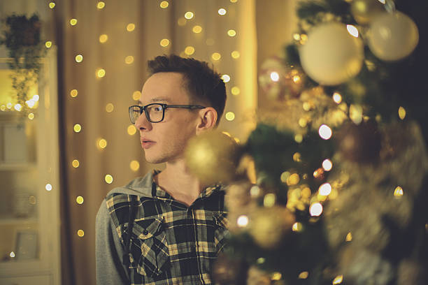 istock Smiling Young Man Peeking from Behind a Festive Christmas Tree 2250533047