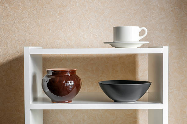 A tidy white kitchen cabinet with open shelves displays plates, bowls, and cups stacked neatly, creating a minimal and organized storage scene in a modern home.