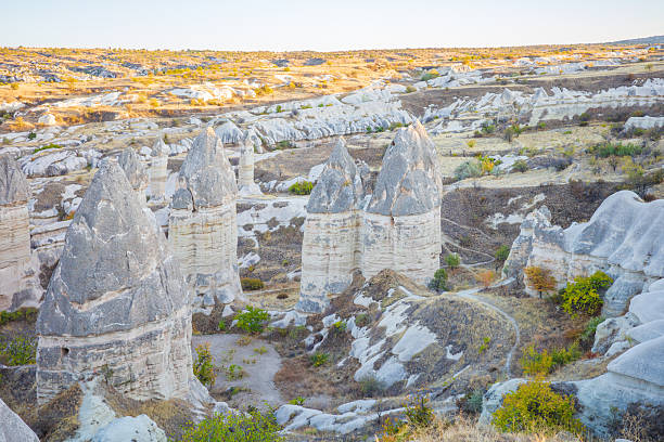 A breathtaking view of Cappadocia’s iconic fairy chimneys and unique rock formations illuminated by warm sunset light. The soft pastel tones, eroded volcanic terrain, and winding natural paths highlight the region’s geological beauty and historic charm. Ideal for themes related to travel, nature, geology, national parks, outdoor adventure, Turkish landscapes, and world heritage destinations. Perfect for editorial use, travel guides, documentaries, posters, and tourism marketing