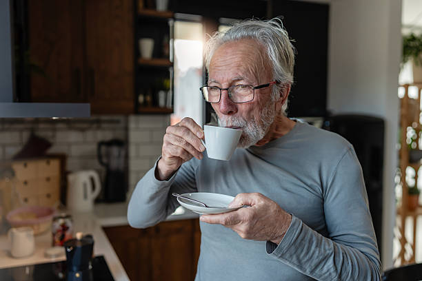 istock Elderly man sipping hot coffee from a cup while standing in a cozy kitchen, enjoying a quiet morning moment 2250554113