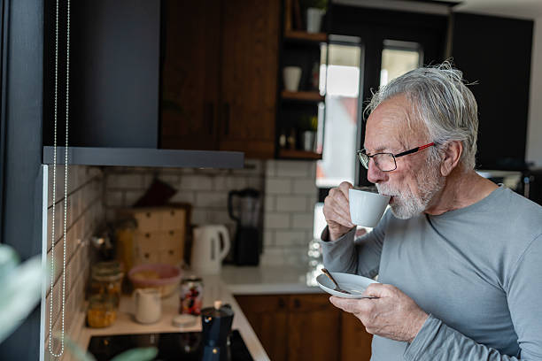 istock Elderly man sipping hot coffee from a cup while standing in a cozy kitchen, enjoying a quiet morning moment 2250554121