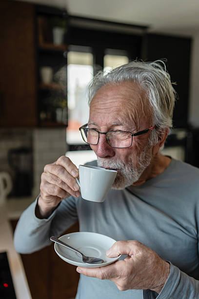 istock Elderly man sipping hot coffee from a cup while standing in a cozy kitchen, enjoying a quiet morning moment 2250554193