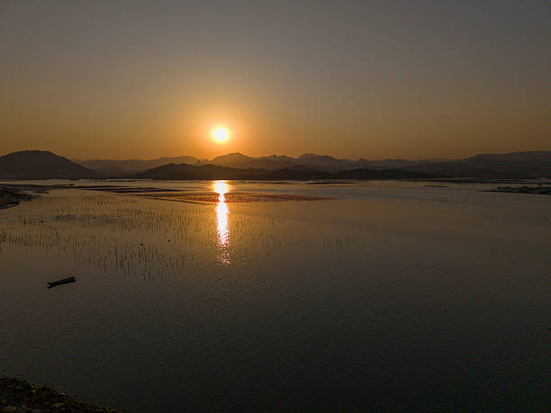 A tranquil sunset scene featuring three boats on calm waters near a mountainous coastline. The warm colors create a peaceful atmosphere, ideal for travel or nature photography.