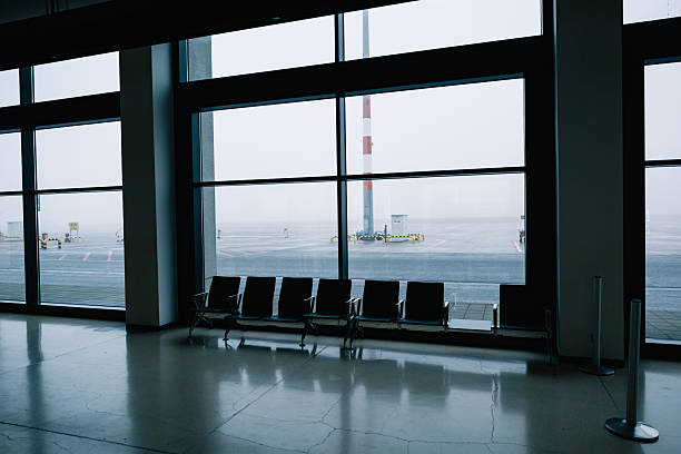 Minimalist airport terminal scene showing empty seats and a mist covered runway outside.