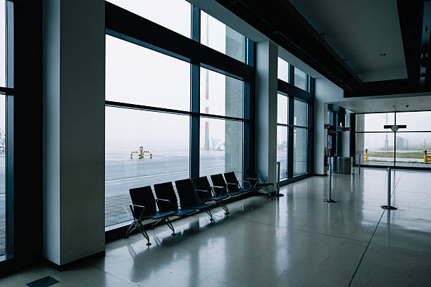 Minimalist airport terminal scene showing empty seats and a mist covered runway outside.
