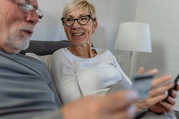 istock Smiling senior couple sitting together at home, using a smartphone for online shopping while holding a credit card 2250560155