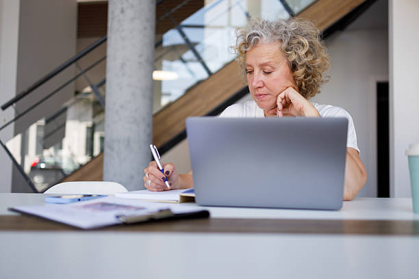 istock Senior businesswoman working in office, writing notes and using laptop, focused on her professional tasks 2250563151