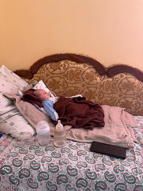 Newborn baby sleeping on bed surrounded by blankets and feeding bottles