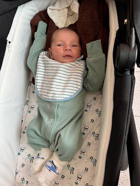 Newborn Baby Resting in Stroller with Raised Arms Indoors