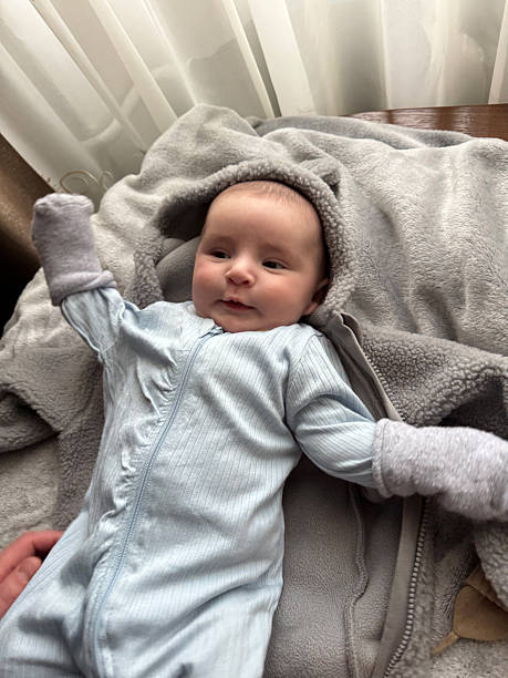 istock Happy Baby in Light Blue Romper Lying on Soft Blanket with Raised Arms 2250571337