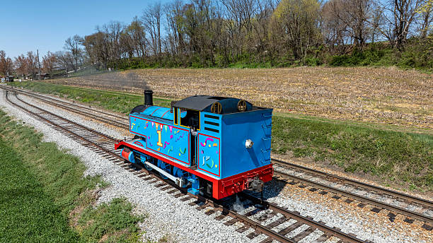 Ronks, Pennsylvania, April 17, 2025 - A colorful vintage train engine is traveling along a railway track surrounded by lush fields. The bright blue and red colors stand out against the green landscape.