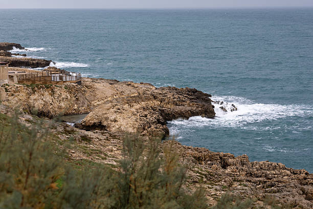 istock moody coastal scene where dramatic, rugged cliffs meet the churning sea under an overcast sky, with a small, rustic wooden viewing deck built into the rocks. 2250579777