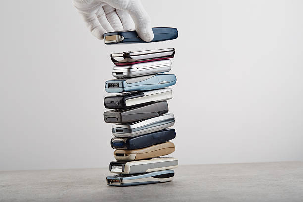 A hand is stacking old, outdated mobile phones on top of each other, e-waste concept
