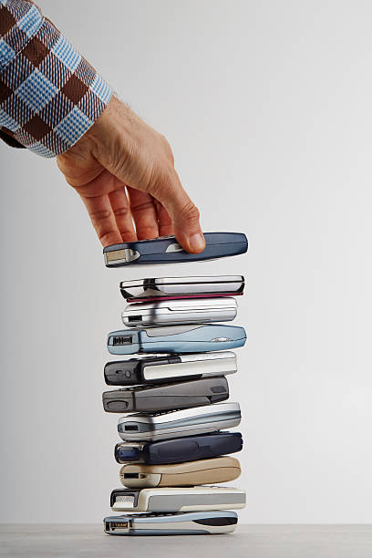 A hand is stacking old, outdated mobile phones on top of each other, e-waste concept