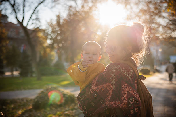 Mother and baby boy enjoying tender moments in public park during sunny autumn day