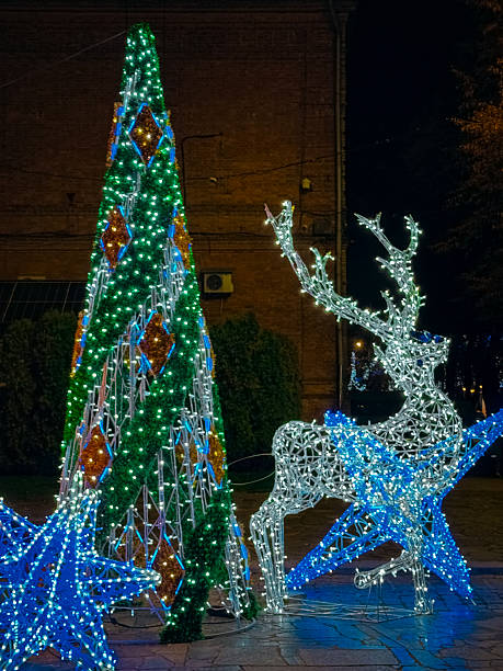istock Outdoor holiday decorations featuring a wireframe LED reindeer, a tall illuminated cone-shaped tree, and glowing blue stars 2250590267