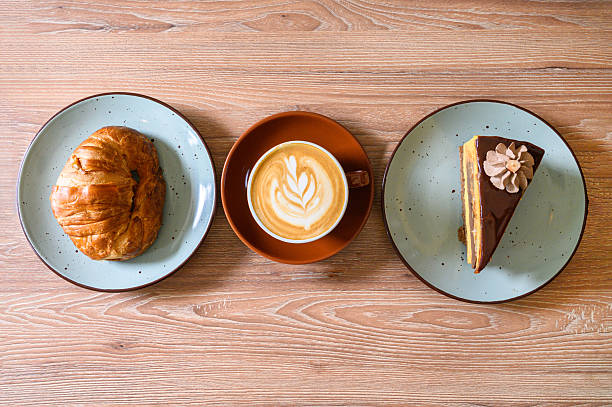 Coffee latte with croissant and chocolate cake on wooden table, top view