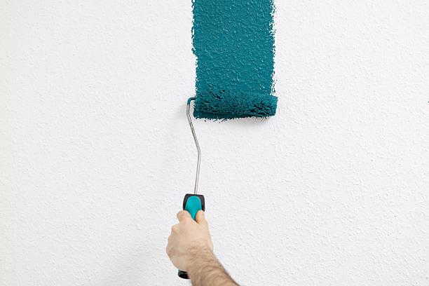 istock Hand holding paint roller applying teal paint on textured wall during home renovation project, showcasing DIY interior design concept 2250606866