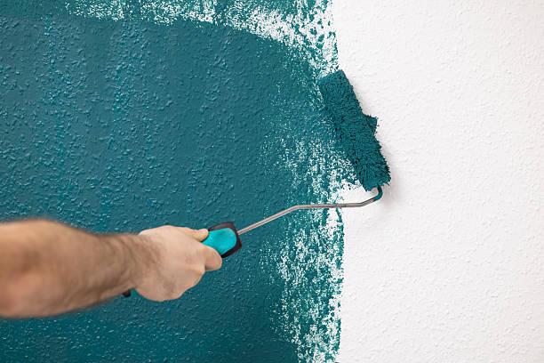 istock Hand holding paint roller applying teal paint on textured wall, showcasing home improvement and creative renovation process with copy space 2250606870