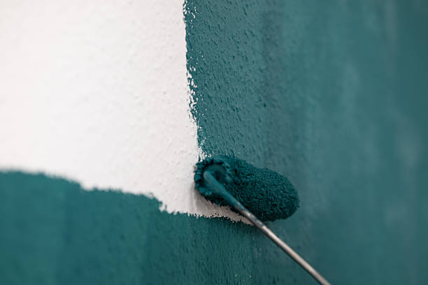 Roller brush is painting a textured wall with teal color, highlighting the transformation of the surface and the artistic process of home improvement