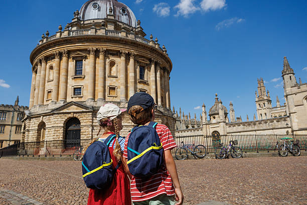 Oxford, United Kingdom - August 14, 2015: Clarendon Building Square and Bridge of Sighs in Oxford with a crowd of tourists with a tour guide. Cloudy day.