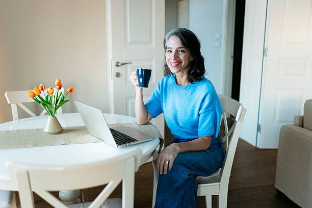 istock Smiling woman working from home using laptop and drinking coffee 2250615500