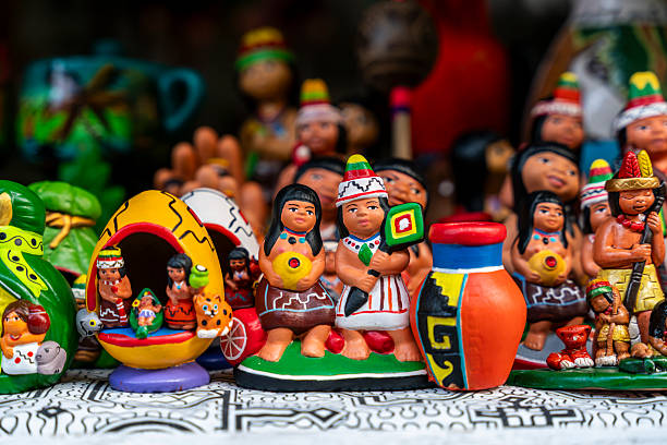 A collection of colorful Amazonian ceramic figures representing Peruvian indigenous culture is displayed on a market table. These handcrafted pieces feature traditional costumes, tribal motifs and vibrant details. Ideal for commercial themes about culture, folklore, craftsmanship, souvenirs and artisans.