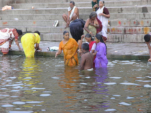 Crowds gather along the Ganges River at a historic ghat in Varanasi - India, engaging in daily rituals, bathing, and communal life. A vibrant scene of tradition, spirituality, and cultural heritage unfolds on the riverbanks.