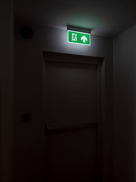 istock Emergency exit door with illuminated green sign in dark hallway symbolizes fire escape, building safety, evacuation route, emergency preparedness, and exit strategy in public spaces. 2250629585