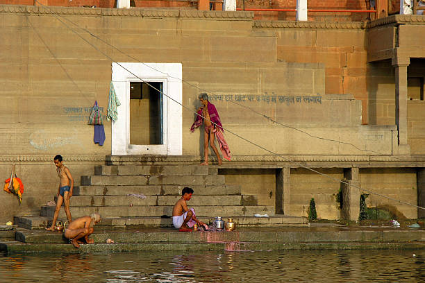 Crowds gather along the Ganges River at a historic ghat in Varanasi - India, engaging in daily rituals, bathing, and communal life. A vibrant scene of tradition, spirituality, and cultural heritage unfolds on the riverbanks.