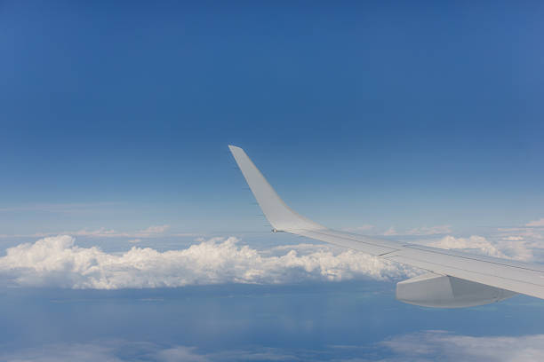 Through plane window blue sky and white cloud background image with white plane wing.