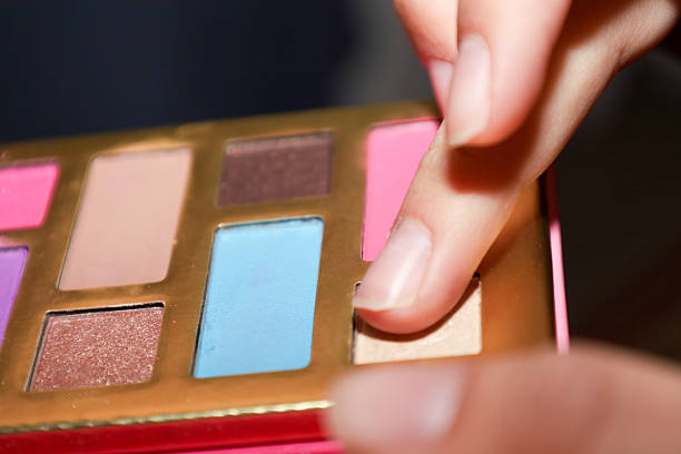 A beautiful macro shot of a hand selecting a shade from a multi-colored eyeshadow palette. The gentle lighting highlights the texture of the cosmetics and the well-maintained nails.