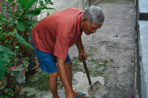 istock Elderly Villager Bending Down to Scoop Swept Debris 2250646007